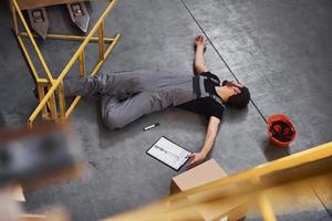 Warehouse worker after an accident in the storage. Man in uniform lying down on the ground photo