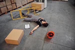 Warehouse worker after an accident in the storage. Man in uniform lying down on the ground photo