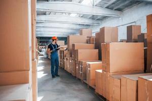 Storage worker in uniform and notepad in hands checks production photo