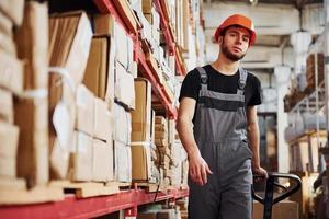 Young male worker in uniform is in the warehouse pushing pallet truck photo