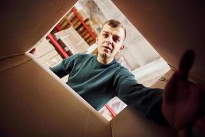 vista desde el interior de la caja de papel. el hombre con ropa informal mira hacia abajo y trata de alcanzar la cámara con la mano foto