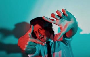 Portrait of young stylish man in hat and with glasses that stands in neon lights in the studio photo