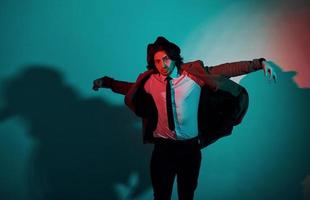 Portrait of young stylish man in hat, suit and tie that stands in neon lights in the studio photo