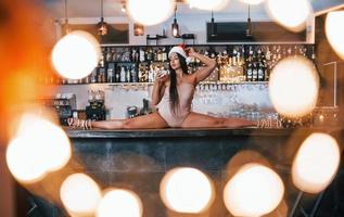 Sexy young woman in new year hat hot clothes sits and doing stretch on the table of restaurant photo