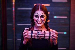 Portrait of woman that is on the thematic halloween party in scary makeup and costume with bomb in hands photo