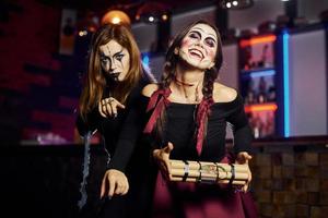 Two female friends is on the thematic halloween party in scary makeup and costumes with time bomb photo