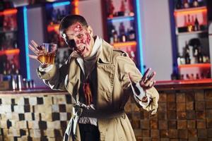 With drink in hand. Portrait of man that is on the thematic halloween party in zombie makeup and costume photo