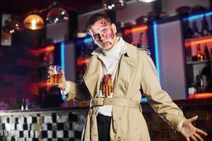 With drink in hand. Portrait of man that is on the thematic halloween party in zombie makeup and costume photo