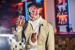 With drink in hand. Portrait of man that is on the thematic halloween party in zombie makeup and costume photo