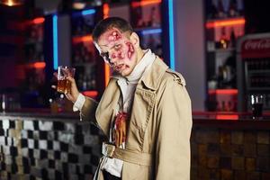 With drink in hand. Portrait of man that is on the thematic halloween party in zombie makeup and costume photo