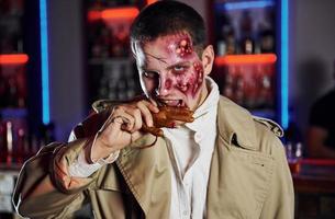 Eating dead hand. Portrait of man that is on the thematic halloween party in zombie makeup and costume photo