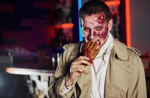 comer mano muerta. retrato de hombre que está en la fiesta temática de halloween con maquillaje y disfraz de zombi foto