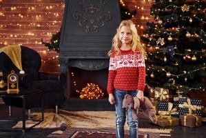 Cute little girl in red festive sweater with teddy bear indoors celebrating new year and christmas holidays photo