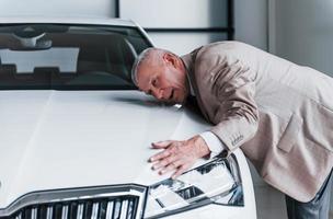 Cheerful aged man in formal wear stands in front of modern white car photo