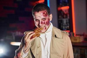 comer mano muerta. retrato de hombre que está en la fiesta temática de halloween con maquillaje y disfraz de zombi foto