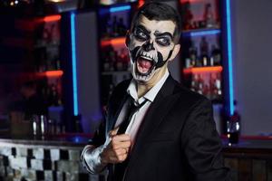 gritando a la cámara. retrato de hombre que está en la fiesta temática de halloween con maquillaje y disfraz de esqueleto aterrador foto