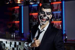 Screaming to the camera. Portrait of man that is on the thematic halloween party in scary skeleton makeup and costume photo