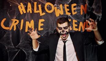 Portrait of man that is on the thematic halloween party in scary skeleton makeup and costume against crime scene wall photo