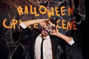 retrato de hombre que está en la fiesta temática de halloween con maquillaje de esqueleto aterrador y disfraz contra la pared de la escena del crimen foto