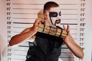 Portrait of man that is on the thematic halloween party in scary black metal makeup and costume with bomb in hands photo