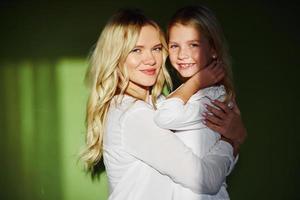 Mother with her daughter together in the studio with green background embracing each other photo