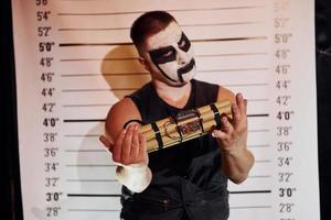 Portrait of man that is on the thematic halloween party in scary black metal makeup and costume with bomb in hands photo