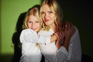 Mother with her daughter together in the studio with green background embracing each other photo