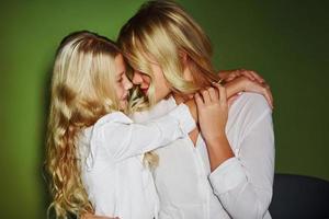 Mother with her daughter together in the studio with green background embracing each other photo