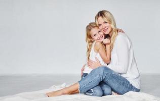 Mother with her daughter together is on the ground in the studio with white background photo