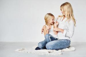 madre con su hija juntas está en el suelo en el estudio con antecedentes blancos foto