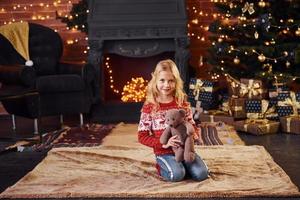 Cute little girl in red festive sweater with teddy bear indoors celebrating new year and christmas holidays photo