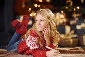 Cute little girl in red festive sweater indoors lying down celebrating new year and christmas holidays photo