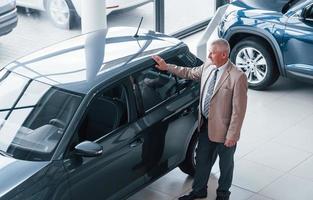 Aged man in formal wear walking in the automobile salon and looking for the car photo