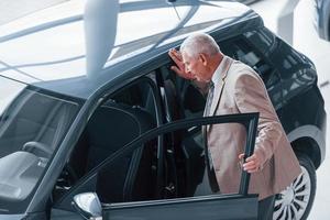 Aged man in formal wear walking in the automobile salon and looking for the car photo