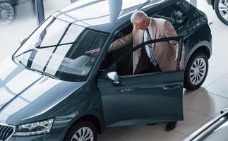 Aged man in formal wear walking in the automobile salon and looking for the car photo