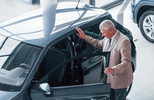 Aged man in formal wear walking in the automobile salon and looking for the car photo