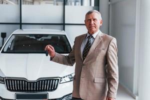 Cheerful aged man in formal wear stands in front of modern white car photo