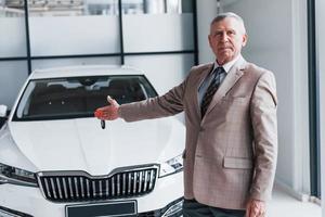 Cheerful aged man in formal wear stands in front of modern white car photo