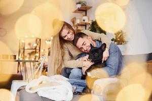 Happy young modern couple sitting on the sofa at home with their cute dog photo