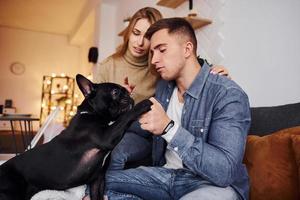 Happy young modern couple sitting on the sofa at home with their cute dog photo