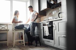 feliz joven pareja moderna en la cocina de casa con su lindo perro foto