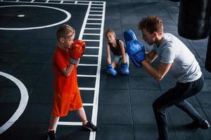 Young trainer teaches kids boxing sport in the gym photo