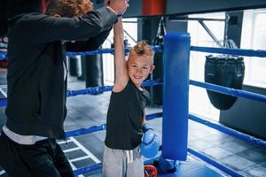 Boxing coach standing in the ring with boy and celebrating victory together photo