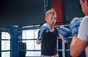 Boy in protective gloves have sparring with trainer on the boxing ring photo