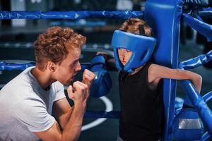 el joven entrenador de boxeo está ayudando a un niño con ropa protectora en el ring entre las rondas foto