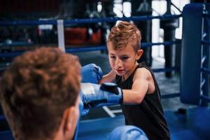 Young boxing coach is helping little boy in protective wear on the ring between the rounds photo