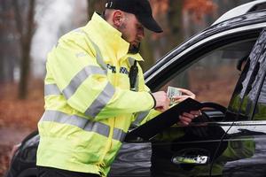 oficial de policía masculino con uniforme verde que acepta sobornos del conductor del vehículo en la carretera foto