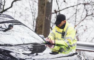 Male police officer in green uniform checking vehicle on the road photo