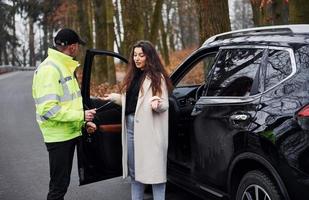 Male police officer in green uniform talking with female owner of the car on the road photo