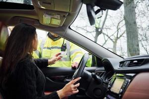 oficial de policía masculino con uniforme verde revisando el vehículo en la carretera. mujer tratando de dar soborno foto